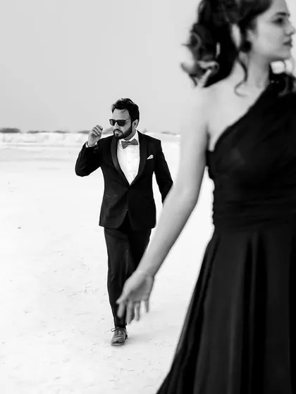 A dramatic, high-fashion pre-wedding shot in a stark, white landscape. The black and white treatment and the composition give it a cinematic, almost surreal quality, like a still from a classic film.
