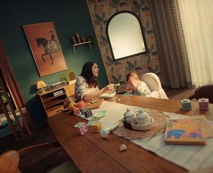 A wider shot showing the chaotic home environment. The mother's simple, practical outfit contrasts with the mess, highlighting her need for help.