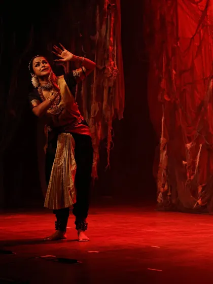 A solo moment on a dramatically lit stage, with a backdrop of tattered red fabric creating a powerful, raw atmosphere for the scene. This is from a performance at the Royal Opera House, Mumbai.