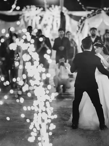 The first dance surrounded by cold pyrotechnics. This black and white photograph freezes a magical moment, highlighting the couple amidst the sparks and the crowd of onlookers.