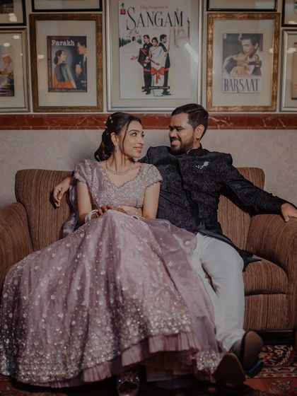 A lovely portrait of the couple on a couch, with classic Bollywood movie posters in the background, adding a fun and unique touch to their Sangeet photos.