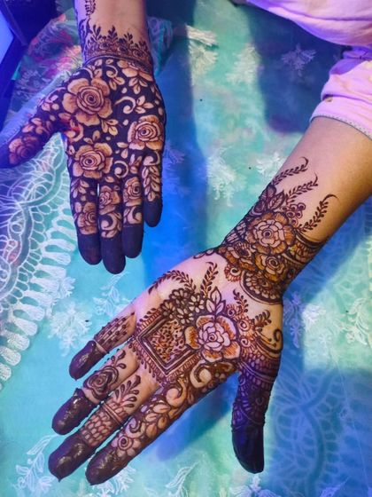 A designer henna piece with one hand featuring a dense floral pattern and the other a bold, modern rose design.