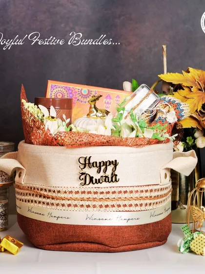 A cozy and rustic "Happy Diwali" hamper in a fabric-lined basket. This gift set includes jars of gourmet treats, a miniature deer figurine, and other festive decor, creating a warm and inviting present for the festival of lights.