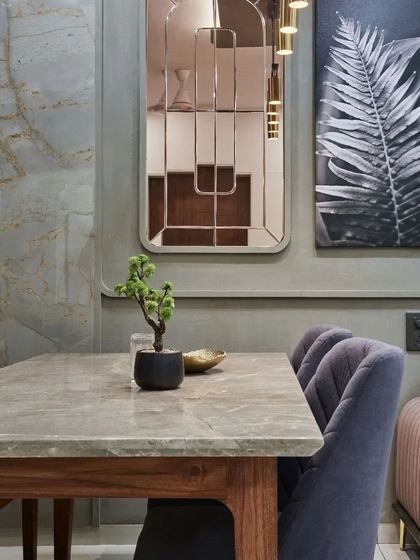 The dining table is set against a textured grey wall, with a small bonsai tree adding a touch of green to the minimalist setting.