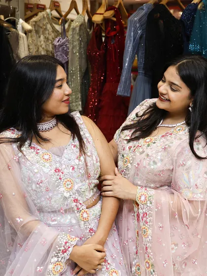 A candid moment between friends, both wearing stunning pastel rental lehengas from my collection.