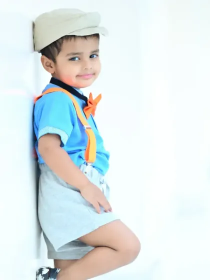 A stylish little boy leaning against a wall outdoors, looking cool and confident.