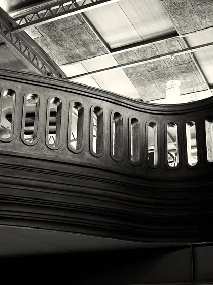 A perspective that showcases the undulating form of the mezzanine railing against the industrial ceiling structure.