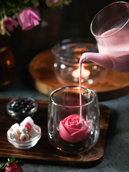 A moody and romantic shot of rose-flavored boba tea being poured into a glass with a rose-shaped ice cube. The dim, candlelit setting and close-up action create an intimate and indulgent atmosphere, perfect for specialty beverage brands.