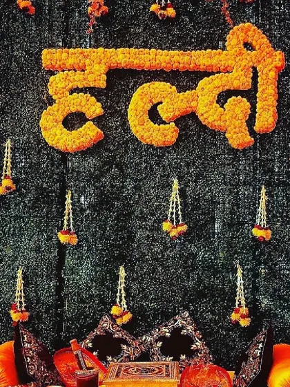 This is a close-up of our signature Haldi ceremony backdrop, a highly requested design for its traditional beauty. We crafted the word "Haldi" in Hindi using dense, fresh marigold flowers, set against a dark green foliage wall. The design is completed with delicate hanging floral tassels, creating a rich, textured look that is perfect for photos.