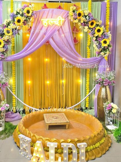 Another view of the lavender and yellow Haldi setup, showing the arrangement of props like bird cages, floral vases, and fun signs like 'Haldi Lagao'.
