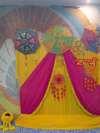 A poolside Haldi decoration with a backdrop of yellow and pink drapes. The decor includes colorful Rajasthani umbrellas and traditional hangings, creating a festive atmosphere.