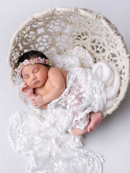 An angelic newborn portrait. The baby is sleeping in a woven basket, draped in flowing white lace.