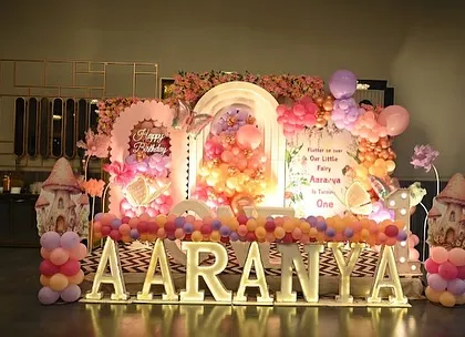 A full stage view for Aaranya's butterfly party, showcasing the large marquee letters, a multi-layered backdrop with a floral ring, and whimsical mushroom props.