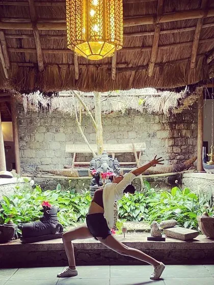 A flowing warrior pose in a tranquil courtyard in Kerala. With a Ganesha statue watching over, this practice becomes a moving meditation, connecting us to the spiritual heritage of the land.