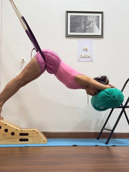 Adho Mukha Svanasana (Downward-Facing Dog) with a rope for sciatica relief. The rope provides traction, extending the lumbar spine and decreasing the compression of the disc on the nerves to reduce pain.