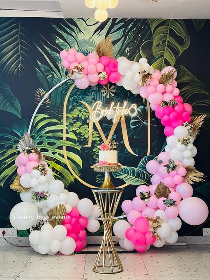 A vibrant "Bride to be" decoration against a tropical leaf wallpaper. The circular gold frame is adorned with a bright pink and white balloon garland, creating a fun and trendy look.