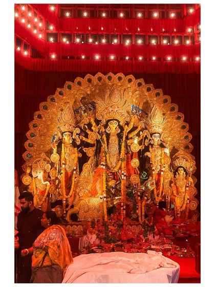 An ornate, golden-themed Durga idol under the warm glow of red lights at a pandal in CR Park, New Delhi.