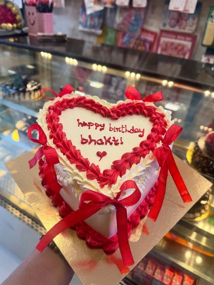 A beautiful heart-shaped cake with red ribbons tied around it. This vintage-style "coquette" cake is a trendy and romantic choice for a special someone's birthday or an anniversary.