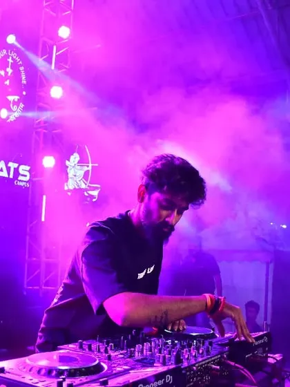 In the zone, mixing tracks on my Pioneer deck under the vibrant purple lights of a packed club. This is where I craft the perfect set, blending beats to keep the dance floor on fire all night.