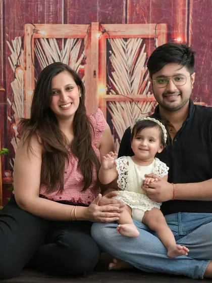 A cozy and rustic family portrait. The wooden backdrop with fairy lights creates a warm and intimate atmosphere for this family of three.