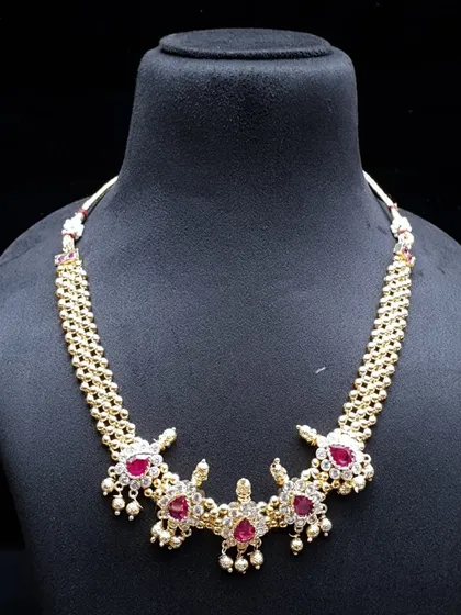 A lovely choker-style necklace made with AD stones and ruby-colored gems. This piece sits beautifully on the neck and is a great choice for pairing with both sarees and gowns.