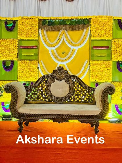 A vibrant yellow and green backdrop for a Seemantham, featuring panels of marigolds and intricate white floral garlands. The ornate sofa provides a perfect centerpiece for the ceremony.