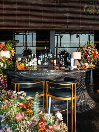 A fully dressed bar surrounded by abundant, colorful floral arrangements. This creates a welcoming and celebratory focal point for guests to gather around.