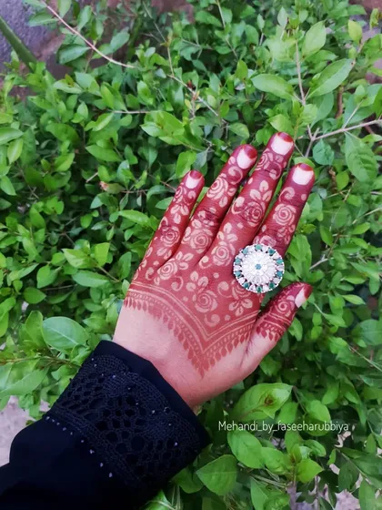A floral party henna design with a beautiful reddish-brown stain, pictured against a natural green background.