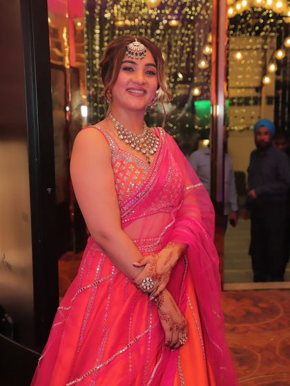 A candid moment from the wedding. The orange and pink lehenga catches the light beautifully, showing the delicate mirror work. The net dupatta is light and easy to manage, which is key for a long event.