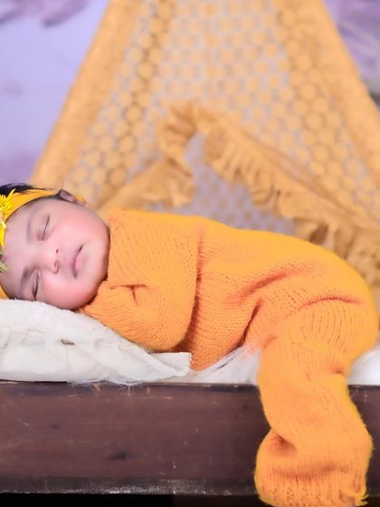 A close-up of a newborn sleeping on a tiny bed, dressed in a warm, knitted outfit. The focus is on their peaceful expression and cozy surroundings.