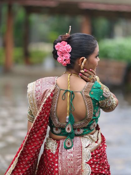 A view of the detailed handwork on the green blouse, paired with a red bandhani-style Nauvari. The hairstyle is adorned with flowers and a traditional 'ambada' pin.