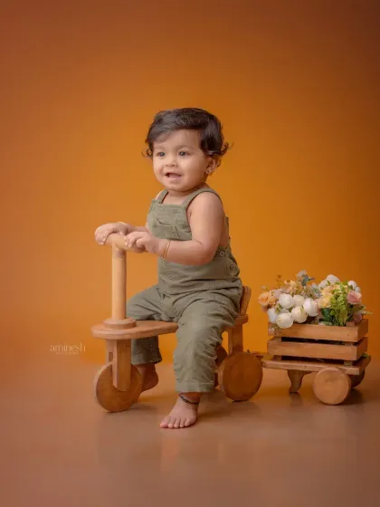 This adorable baby boy in overalls is captured mid-laugh while sitting on a wooden tricycle. These simple prop setups are great for capturing natural expressions.