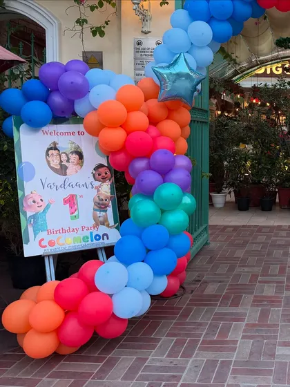 A vibrant, rainbow-colored balloon garland marks the entrance to Vardaan's Cocomelon-themed first birthday party.
