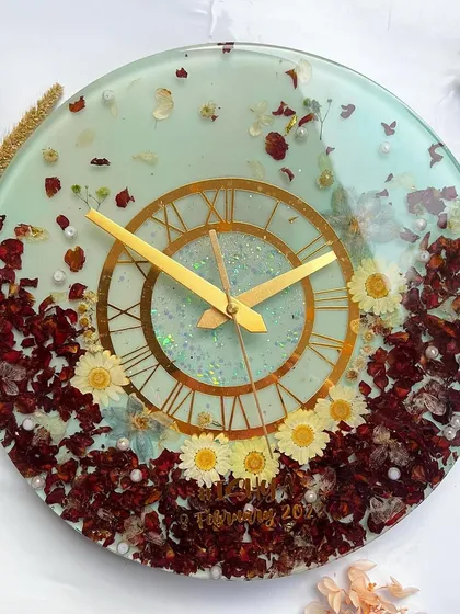 This 12-inch clock features a beautiful combination of preserved red roses and white daisies against a light blue-green resin, creating a fresh, garden-like feel.