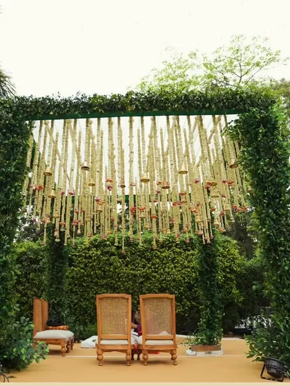 A frontal view of our green mandap, showcasing the two chairs for the couple. The hanging floral strings, known as kaleeras, add a traditional and delicate touch to the natural design.