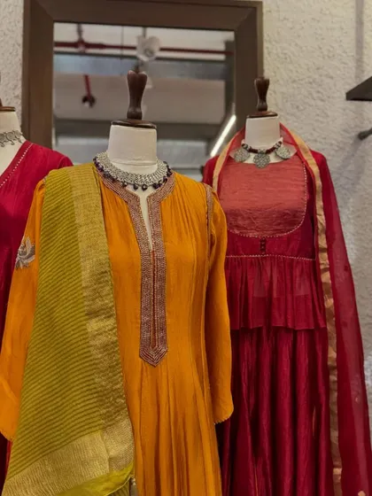 A focus on the orange anarkali, with its intricately embroidered yoke and contrasting striped dupatta, accessorized with a layered silver necklace.