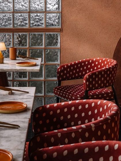 A detail of the seating at Idylll, showcasing the contrast between the patterned fabric, the smooth marble tabletops, and the textured glass block wall.