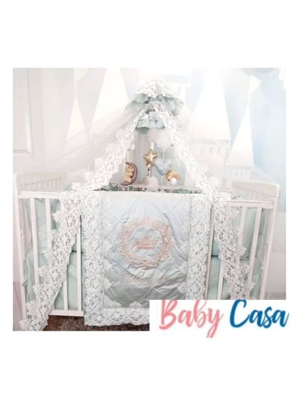 An ethereal and elegant bedding set in a soft mint green. The design is elevated by intricate white lace trim on the quilt, bumpers, and a beautiful canopy.