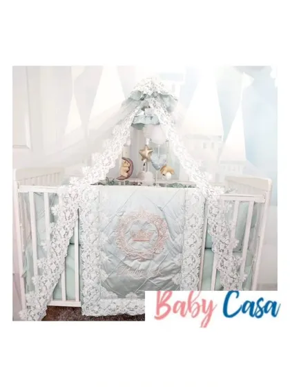 An ethereal and elegant bedding set in a soft mint green. The design is elevated by intricate white lace trim on the quilt, bumpers, and a beautiful canopy.