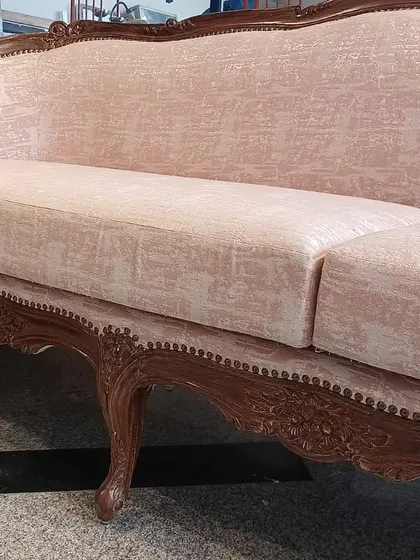A close-up of the hand-carved details on the vintage-style pink sofa. The intricate floral motifs on the wooden legs and frame showcase the high level of craftsmanship that goes into each piece.