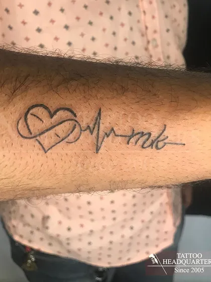 A tattoo combining an infinity symbol, a heart, and a heartbeat line with the initials "MK."