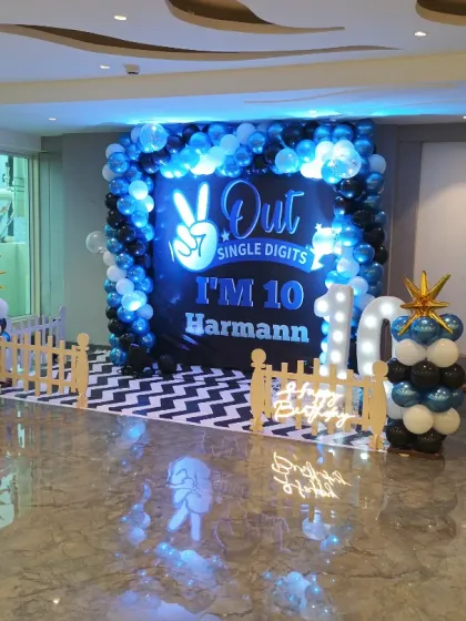 A stylish blue, black, and white balloon backdrop for a 10th birthday party. The setup includes marquee lights for the age and a custom floor print to complete the look.
