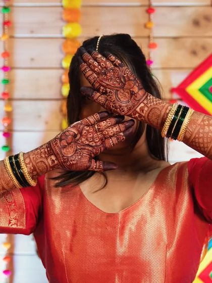 A bride posing against a festive backdrop, her hands adorned with a deep and rich mehendi stain.