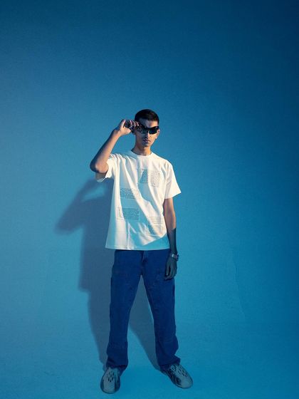 A full-length shot with dramatic, hard-edged shadows. The minimalist composition and the model's pose create a powerful, graphic image.