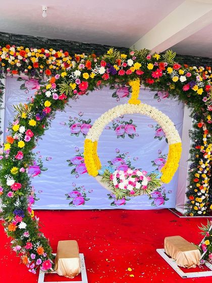 A vibrant and colorful photo booth or backdrop for a fun celebration. The arch is made of multi-colored flowers, with a hanging floral ring for guests to pose with.