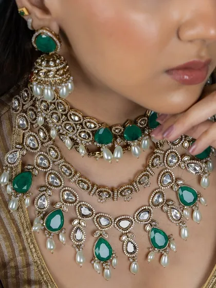 A detailed shot of the layered emerald Kundan necklaces. This view highlights the craftsmanship in the setting of the stones and the delicate pearl drops, perfect for a summer wedding.