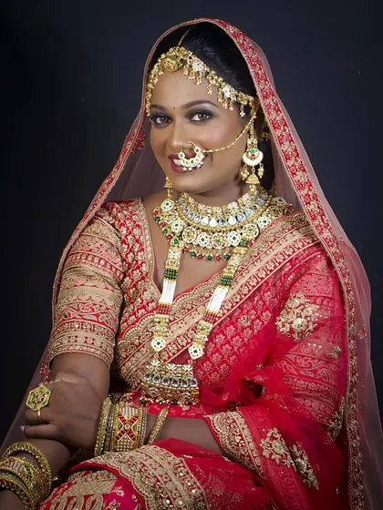 A regal North Indian bride in a classic red lehenga. The makeup is kept timeless with defined eyes and a bold lip, complemented by a matha patti and nath.