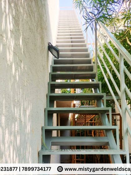 A full view of the outdoor metal staircase, showing how it provides practical access to an upper level. The grey powder-coated finish ensures it is protected from the elements and will last for years.