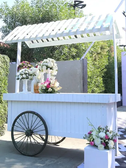 A classic white cart, perfect for serving drinks or desserts, adorned with flowers to fit the chic and clean aesthetic of the carnival.