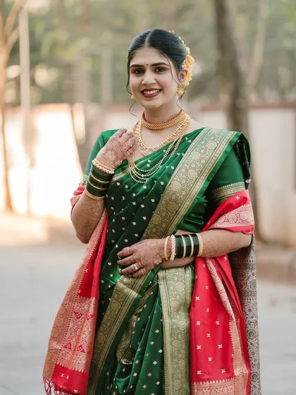 A classic three-quarter portrait of a smiling Marathi bride. The soft outdoor lighting beautifully illuminates her green and red saree and gold jewelry.